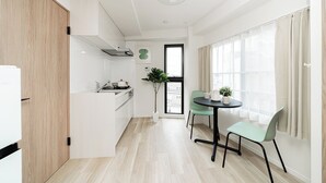 A modern kitchen with a dining area, a potted plant, and a view through a window. - Sunlit Canopy (Shinjuku)