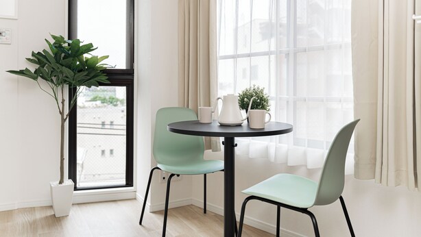 A room with a round table, two chairs, a potted plant, and a window with curtains. - Sunlit Canopy (Shinjuku)