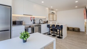 Une cuisine moderne équipée d’un four à micro-ondes, d’un four et d’un évier intégrés. On y trouve également un coin repas avec une table et des chaises blanches.