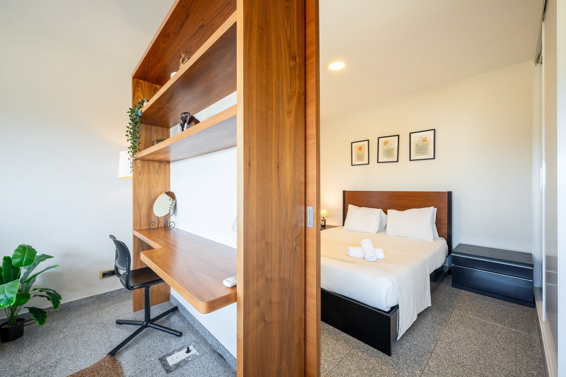 Une chambre d’hôtel avec un lit, un bureau, une chaise et une plante en pot.