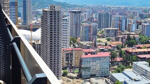 Paisagem urbana com arranha-céus, guindastes de construção e montanhas ao fundo.