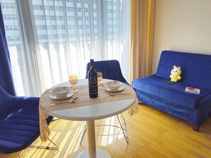 Ein Esstisch mit Flasche, Tellern und Schüssel, ein Plüschtier und ein blaues Sofa in einem Zimmer mit Blick durch ein Fenster.