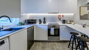 Une cuisine moderne équipée d’un lave-vaisselle, d’un four à micro-ondes, d’une cuisinière et de tabourets de bar.