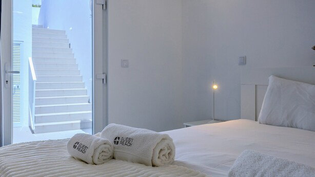 Une chambre d’hôtel avec un lit, deux serviettes enroulées, une table de chevet, une lampe de chevet et une vue sur un escalier.