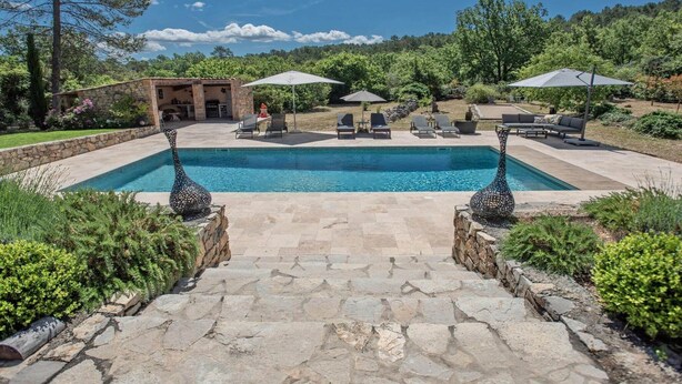 Ein Pool mit Liegestühlen und Sonnenschirmen, umgeben von Steinmauern und Grünpflanzen.