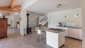 Eine geräumige Küche mit einer zentralen Kochinsel, Holzbalken und einer Treppe zu einer oberen Ebene.