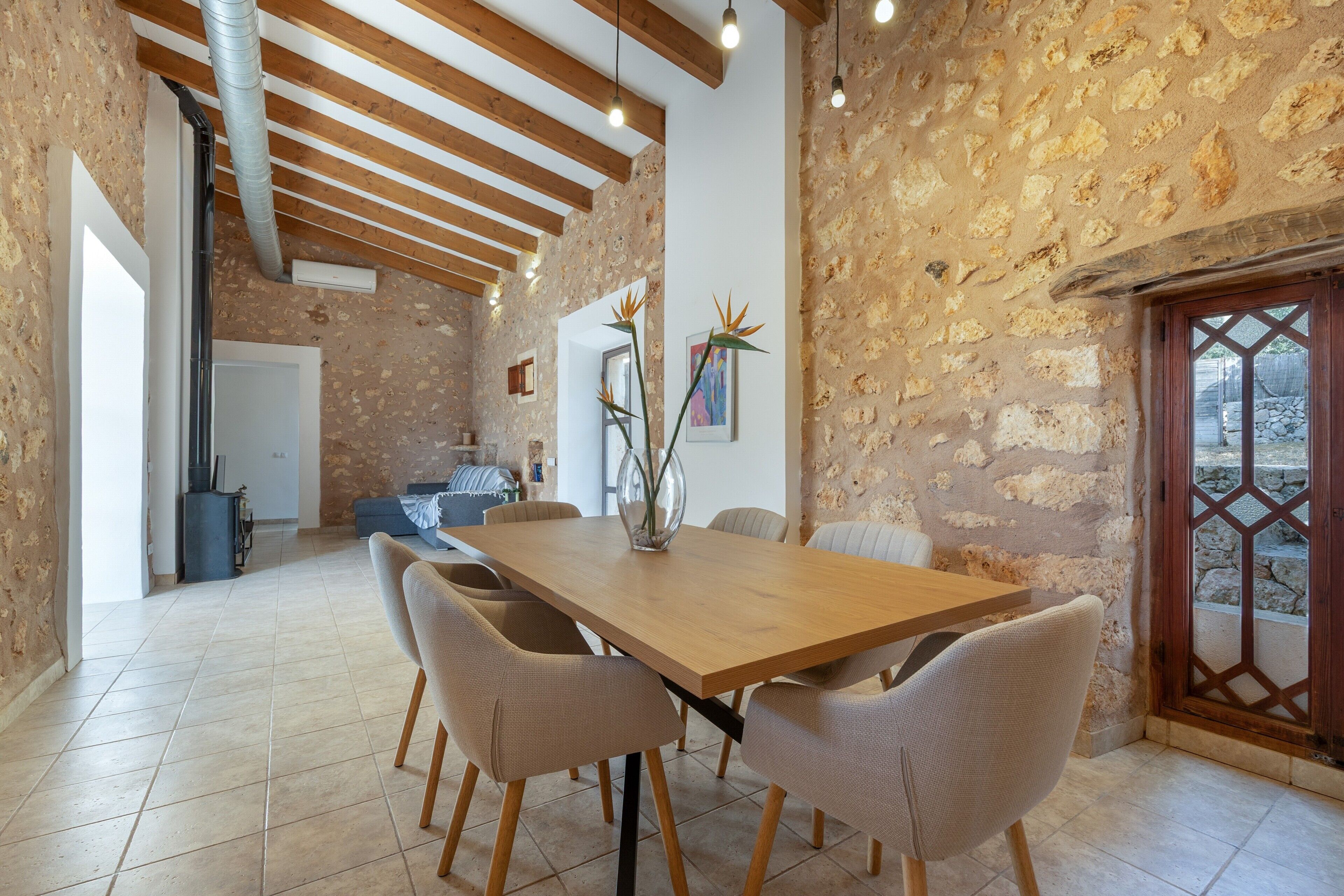 Un comedor con una mesa y sillas de madera, una pared de piedra y vista a través de una puerta de madera.