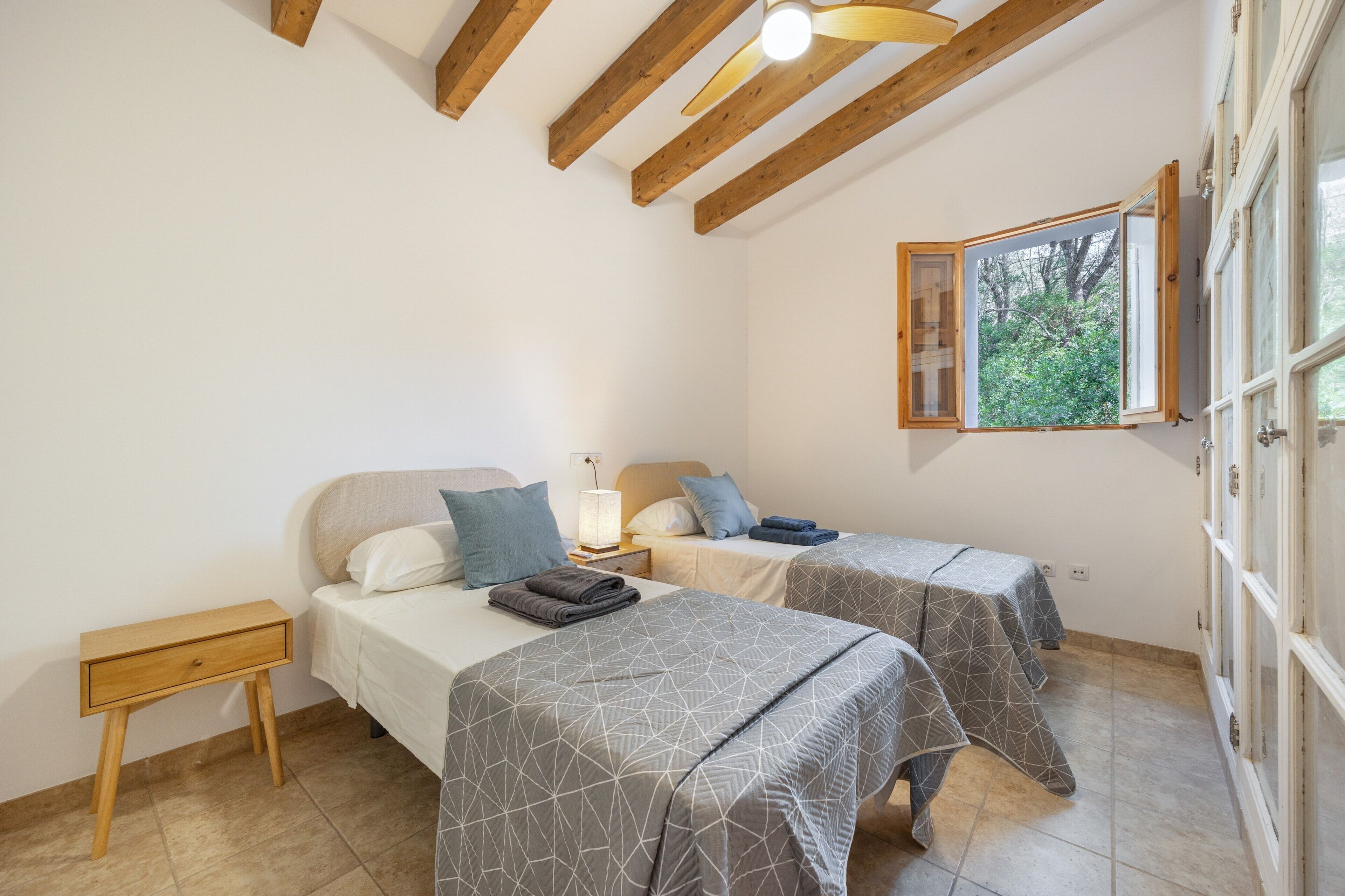 Un dormitorio con dos camas, techo de madera, ventana con vistas y una mesita de noche.