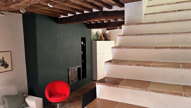 Eine Treppe mit modernem Design, ein roter Sessel und eine dunkle Wand mit Regal.