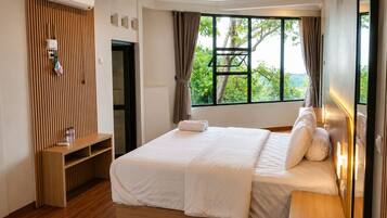 Habitación de hotel con cama, repisa de madera, ventana con cortinas y vista a vegetación.