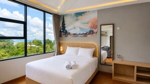 A hotel room with a large bed, a wooden bedside table, a mirror, and a painting of a mountain landscape.