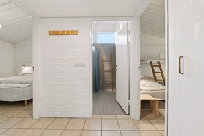 Et rum med en hvid murstensvæg, en seng med træsengegavl, en stige og en dør der fører til et andet rum.