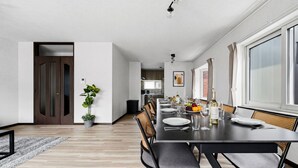 Un comedor moderno con una mesa larga dispuesta para seis comensales, una planta en maceta y vistas de la cocina al fondo.