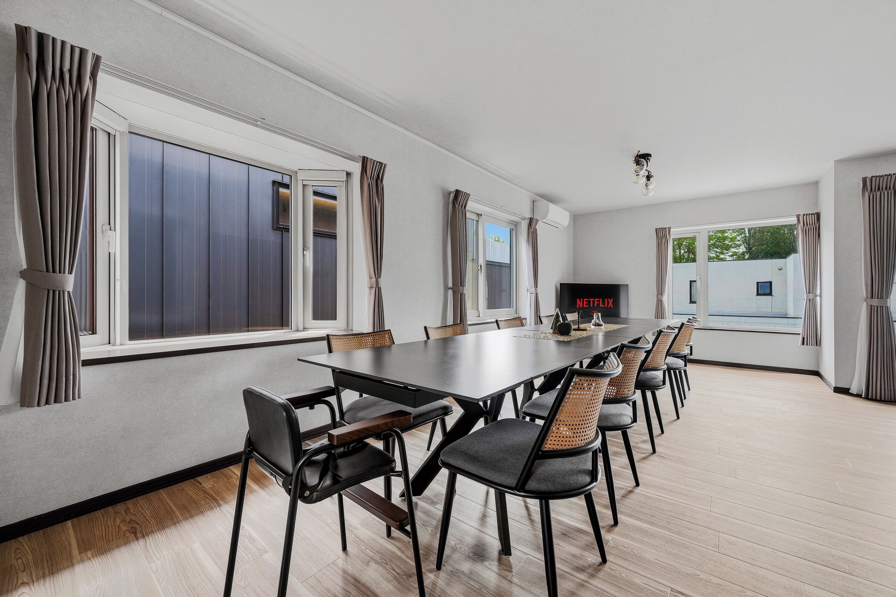Et moderne spiseområde med et langt bord, flere stole og store vinduer.