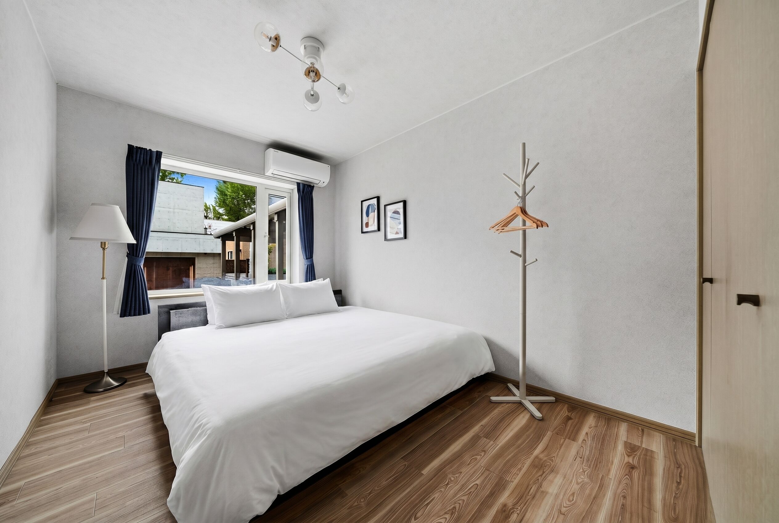 Ein Hotelzimmer mit einem Bett, einer Stehlampe, einem Kleiderständer und einem Fenster mit Vorhängen.