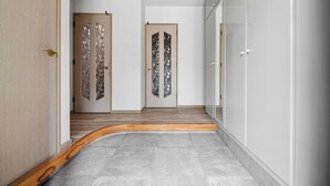 Un pasillo con suelo de madera curvada, dos puertas con paneles de vidrio decorativo y una pared blanca con un armario.