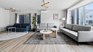Una sala de estar moderna con un sofá, dos mesas auxiliares, una lámpara de pie y un ventanal grande.