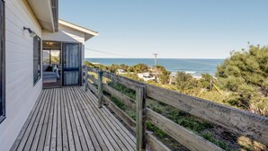 Une terrasse en bois offrant une vue sur l’océan, un bâtiment blanc doté d’une porte-fenêtre coulissante et une clôture en bois.