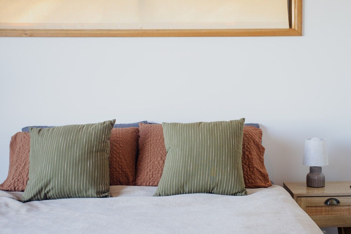 Una cama con almohadas a rayas, una mesita de noche con una lámpara y un cuadro enmarcado sobre la cama.