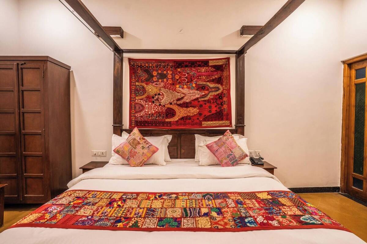 A bedroom with a large bed, a headboard with a tapestry, and a wooden wardrobe.