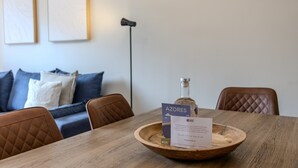 Ein Holztisch mit einer Flasche und einer Karte, ein brauner Ledersessel, ein blaues Sofa und eine Stehlampe in einem modernen Raum.