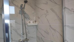 A shower with a handheld showerhead and a wall-mounted faucet, a small shelf with toiletries, and a glass shower door.