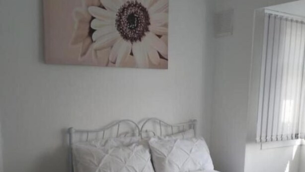 A bedroom with a bed, a headboard, a window with blinds, and a wall-mounted painting.
