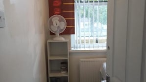 A narrow hallway with a white door marked with the number 1, a radiator, a window with bars, and a fan on a shelf.