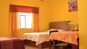 A room with two beds, a table with a lamp, a window with curtains, and a painting on the wall.