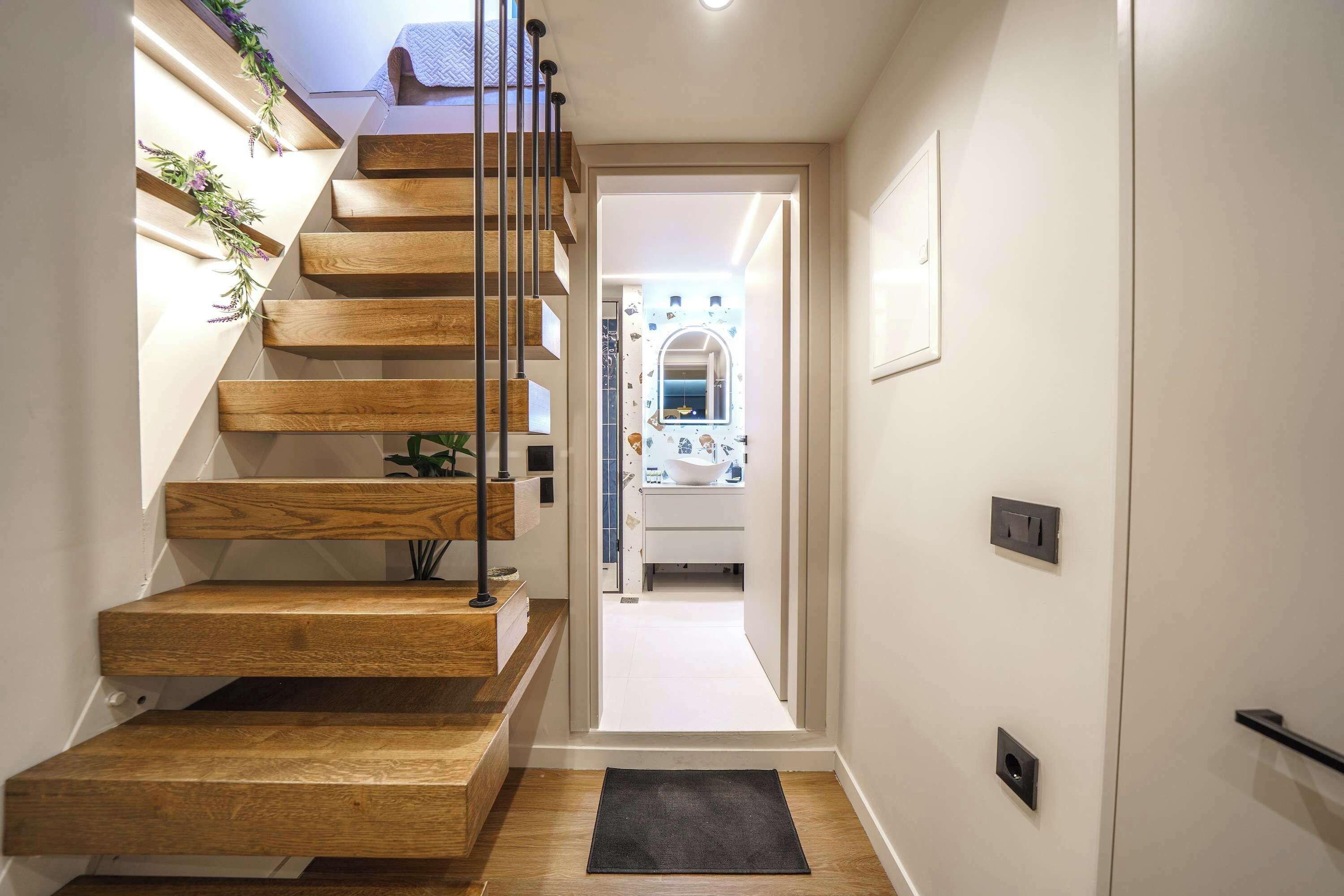 A wooden staircase with a black doormat at the bottom, leading to a doorway.
