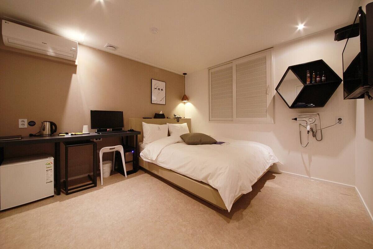 A hotel room with a bed, desk, chair, air conditioning unit, and a wall-mounted TV.