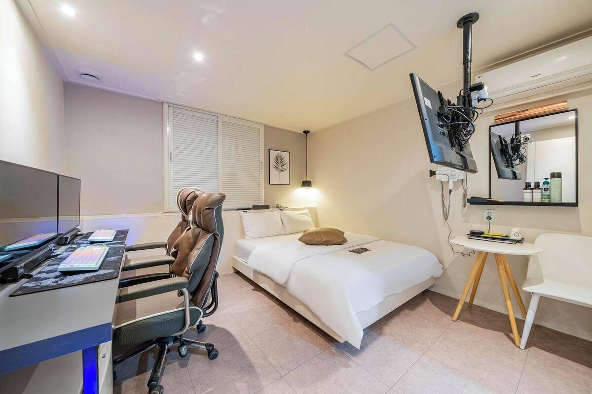 A hotel room with a bed, desk, chair, TV, and a small table.