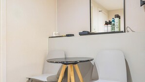 A small room with a round table and two chairs, a mirror, and a shelf with toiletries.