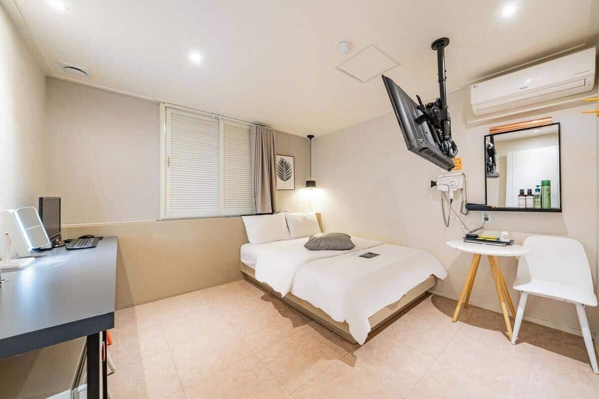 A bedroom with a bed, desk, chair, and a TV mounted on the wall.