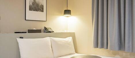 Quarto de hotel com uma cama, abajur, telefone e um quadro na parede.