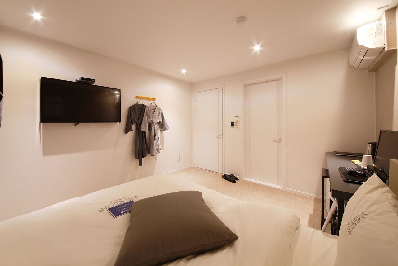 A hotel room with a bed, a flat-screen TV, a desk with a computer, and a wardrobe.