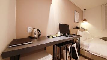 Habitación de hotel con escritorio, cama, silla, mesita, hervidor de agua, ordenador portátil, un cuadro en la pared y ventana.