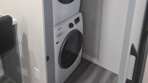 Ein kleiner Waschraum mit zwei gestapelten Waschmaschinen und Trocknern, einem grauen Boden und einer weißen Wand.