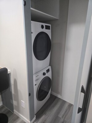 A compact laundry room with two stacked washers and dryers, a gray floor, and a white wall. - Relax in this beautiful ,modern 2-bedroom basement suite in a quiet neighborhood (Edmonton)