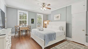 Een slaapkamer met een bed, een bureau, een stoel, een plafondventilator en een deur.