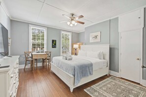 A bedroom with a bed, a desk, a chair, a ceiling fan, and a door. - Charming downtown apartment just steps to King Street (Charleston)