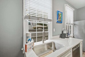 A kitchen with a stainless steel sink, white countertops, and a window with blinds. - Charming downtown apartment just steps to King Street (Charleston)