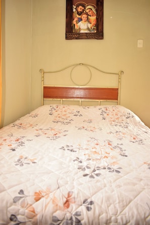 Ein Bett mit floraler Bettdecke, einem hölzernen Kopfteil und einem gerahmten Bild darüber.