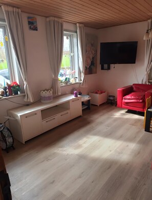 A living room with a white entertainment unit, a red sofa, and a TV mounted on the wall. - A charming, child-friendly house/holiday home. (Øster Assels)