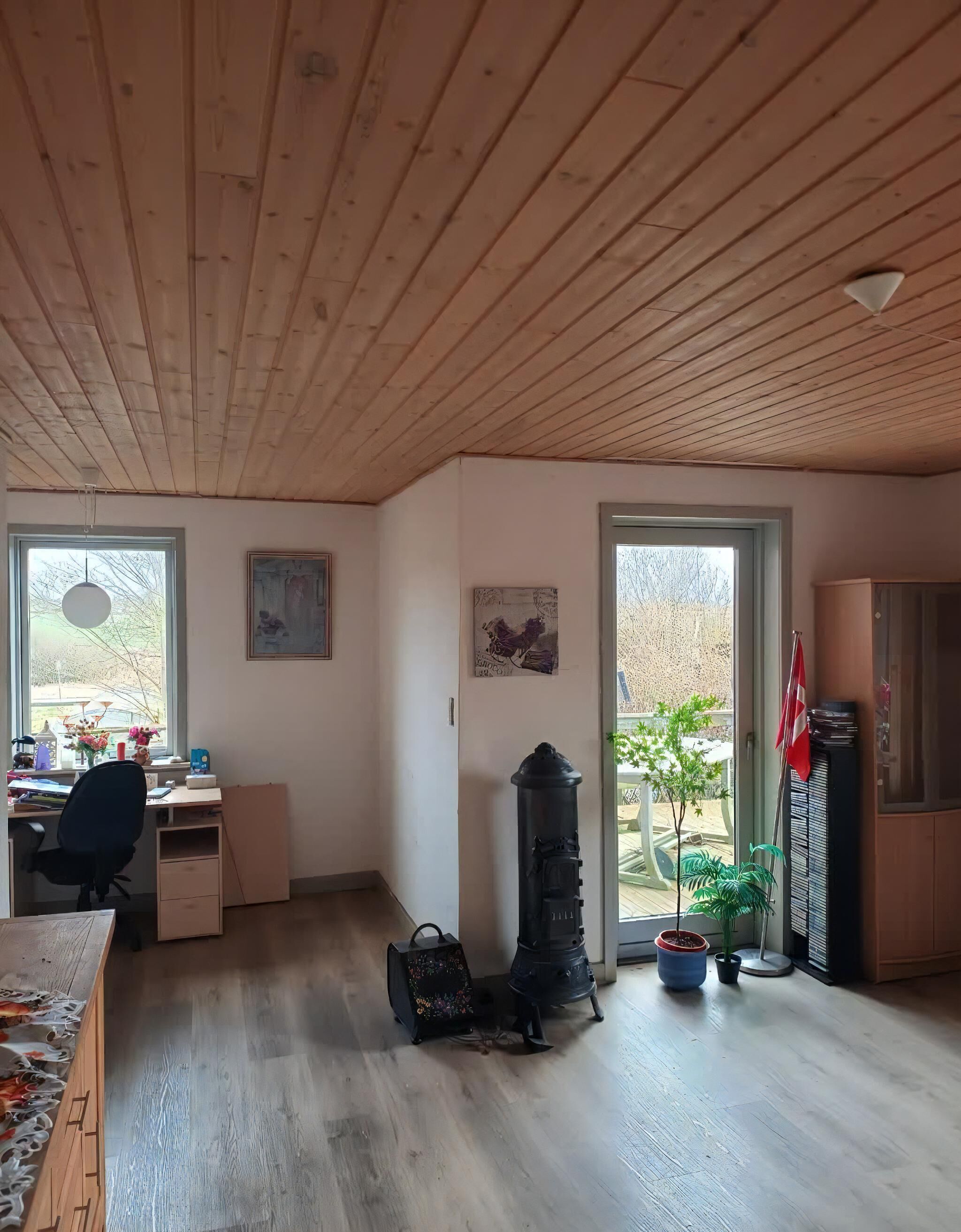 Une pièce avec un plafond en bois, un bureau avec une chaise, un radiateur et une plante en pot.