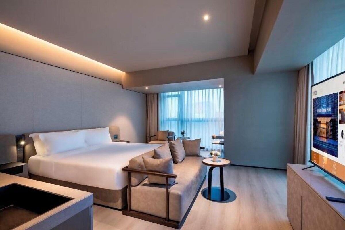 A modern hotel room with a large bed, a sofa, a small round table, and a TV.