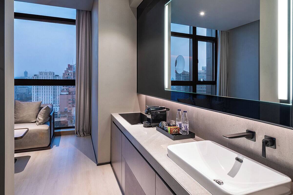 Un baño moderno con un espejo grande, un lavabo y una ventana con vistas a la ciudad.