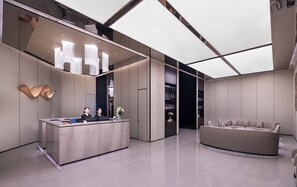 A modern reception area with a reception desk, two staff members, a sofa, and a large window. - Crystal Orange Hotel Xihu Hubin Intime (Hangzhou)