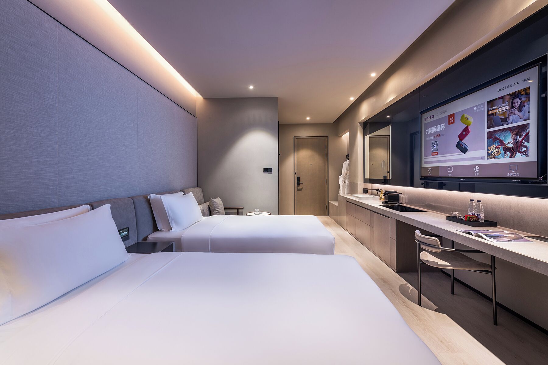 Una habitación de hotel moderna con dos camas, un escritorio y una pantalla de televisión grande.