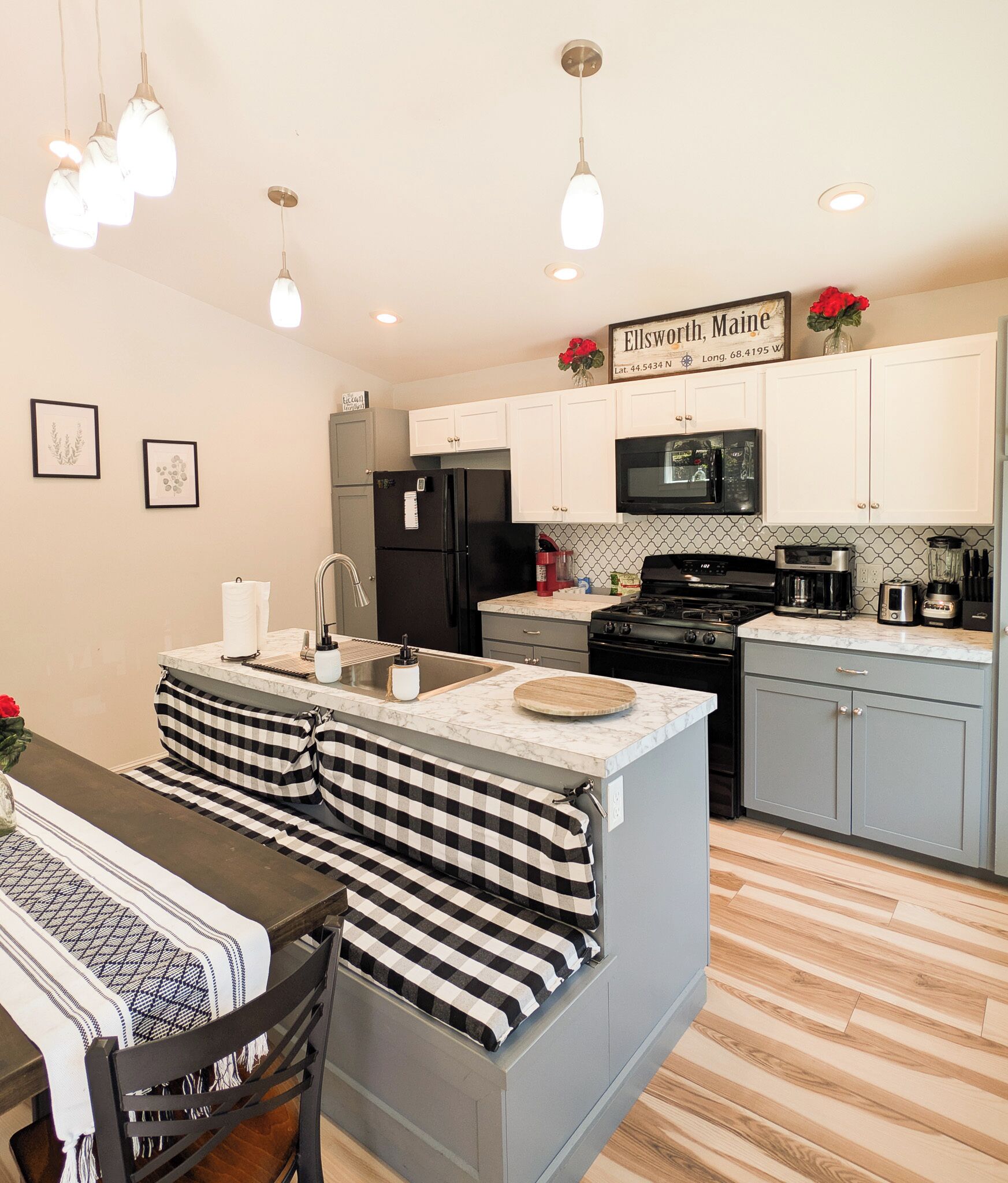 A modern kitchen with a central island, black appliances, white cabinets, and a sign indicating the location.